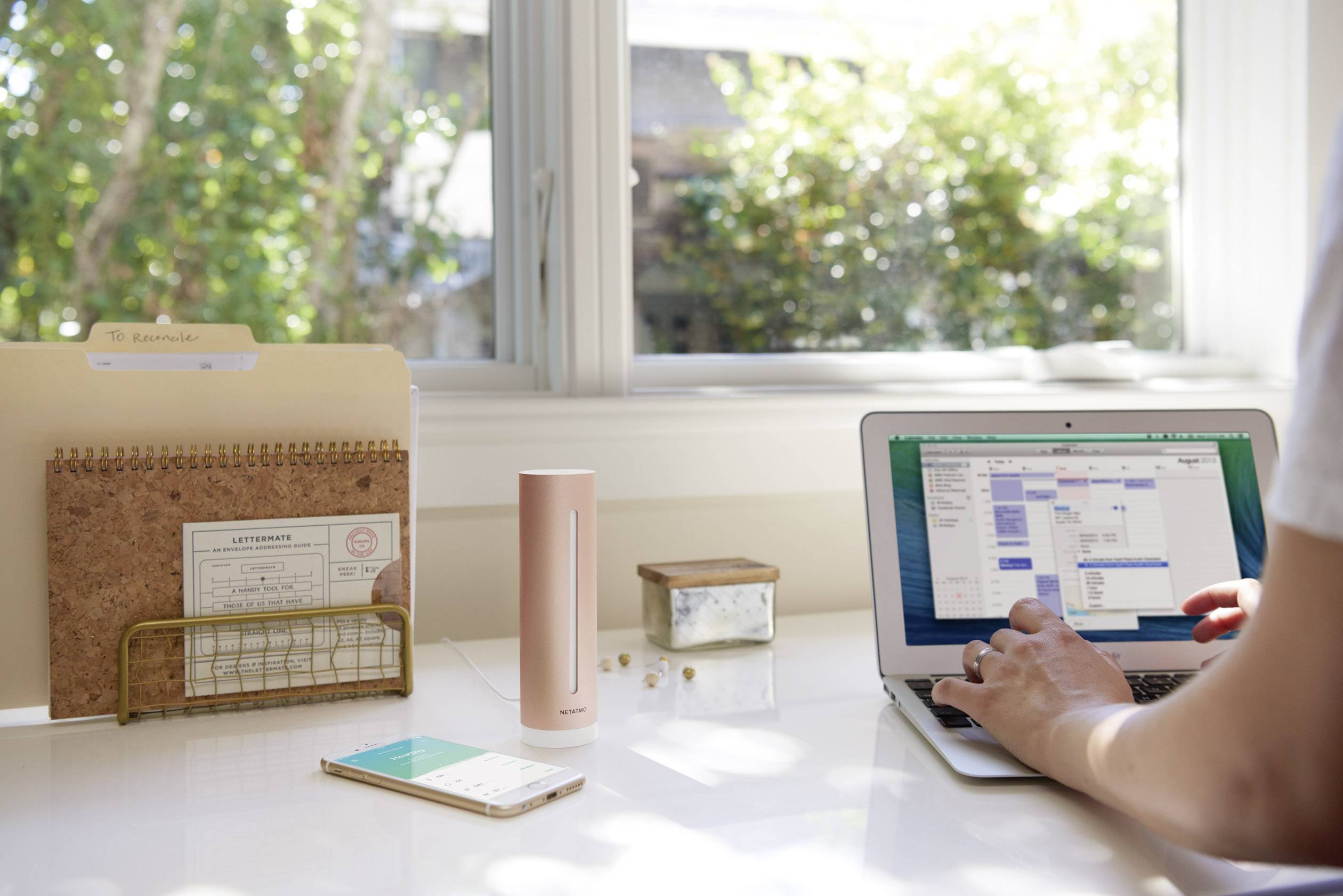 Een persoon werkt op een laptop aan een bureau, omringd door een smartphone, een map en een decoratief voorwerp.