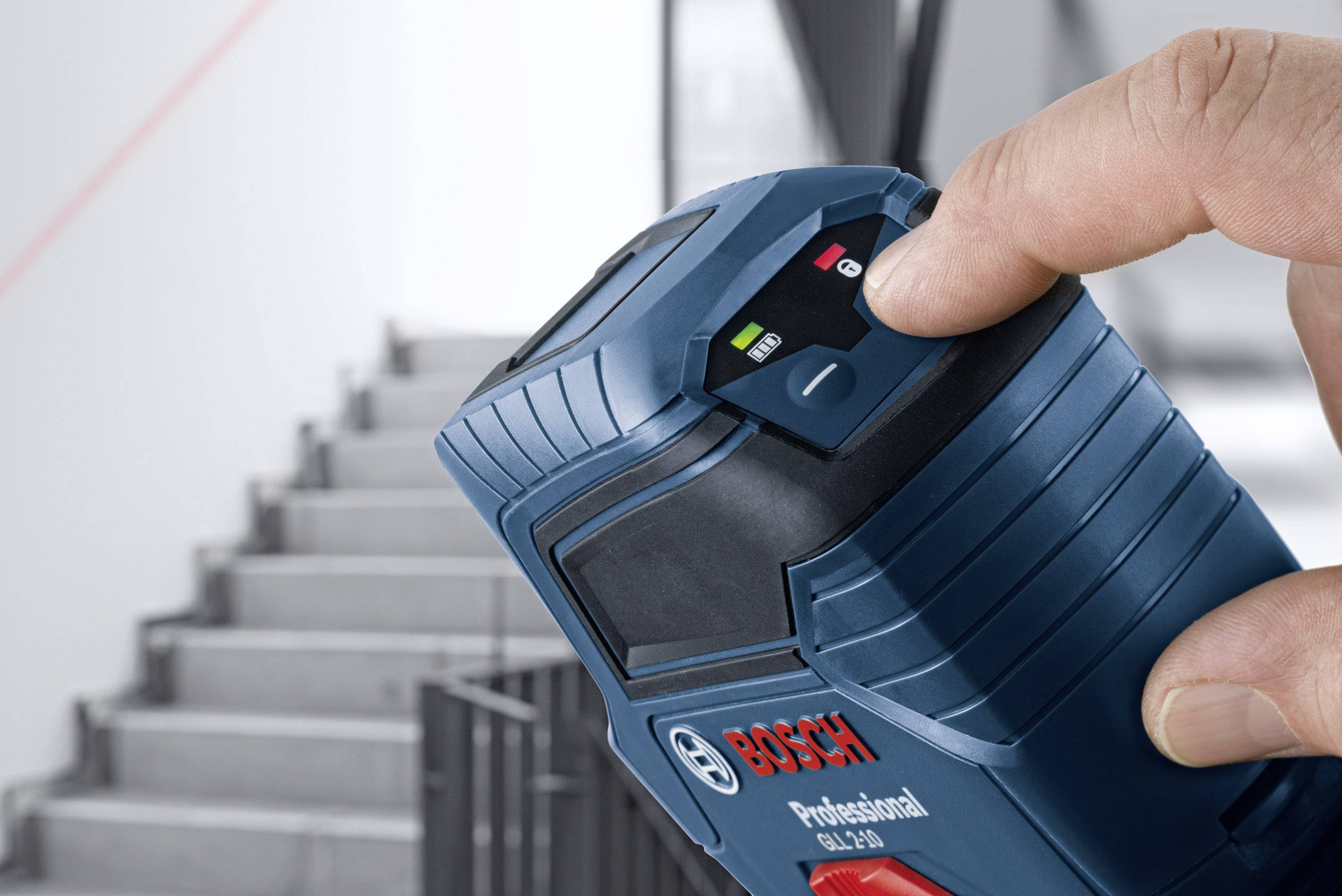 Hand houdt een Bosch-afstandsmeter vast, gericht op een trap, met zichtbaar display en laserstraal op de achtergrond.