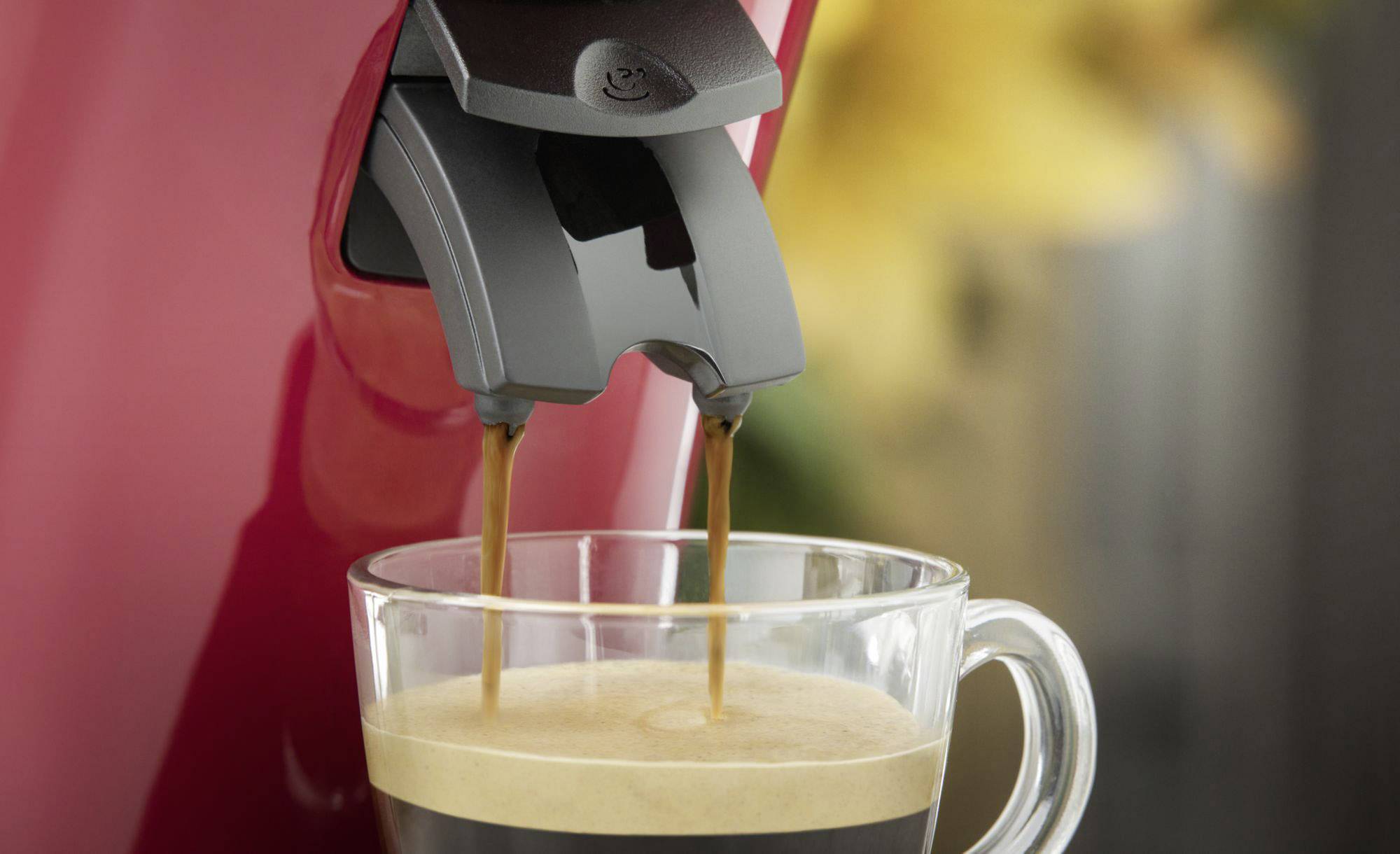 Een koffiemachine giet hete espresso in een transparante kop.