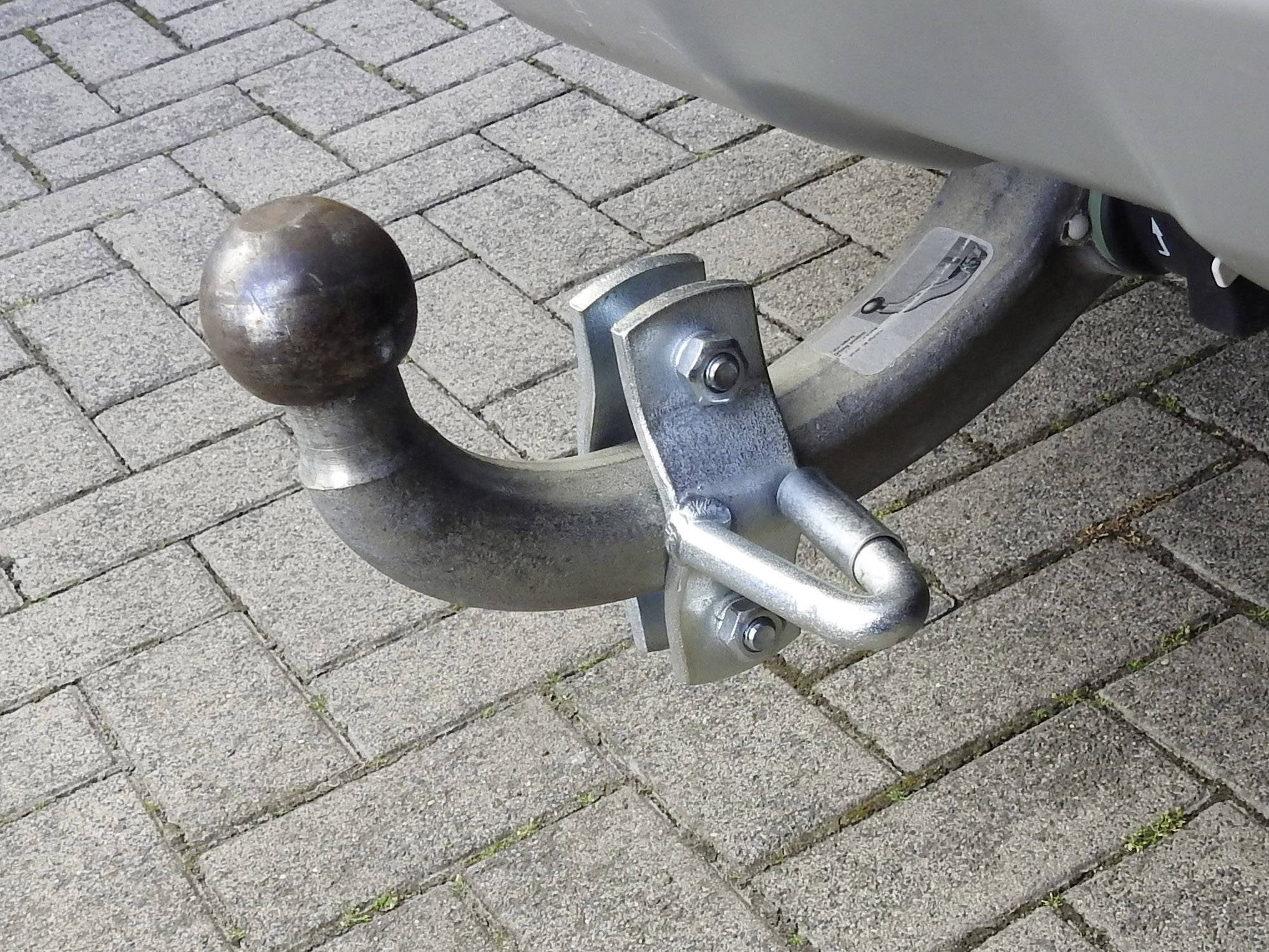 Een aanhangwagenkoppeling aan een geparkeerde auto op klinkers, klaar om verbonden te worden met een aanhanger.