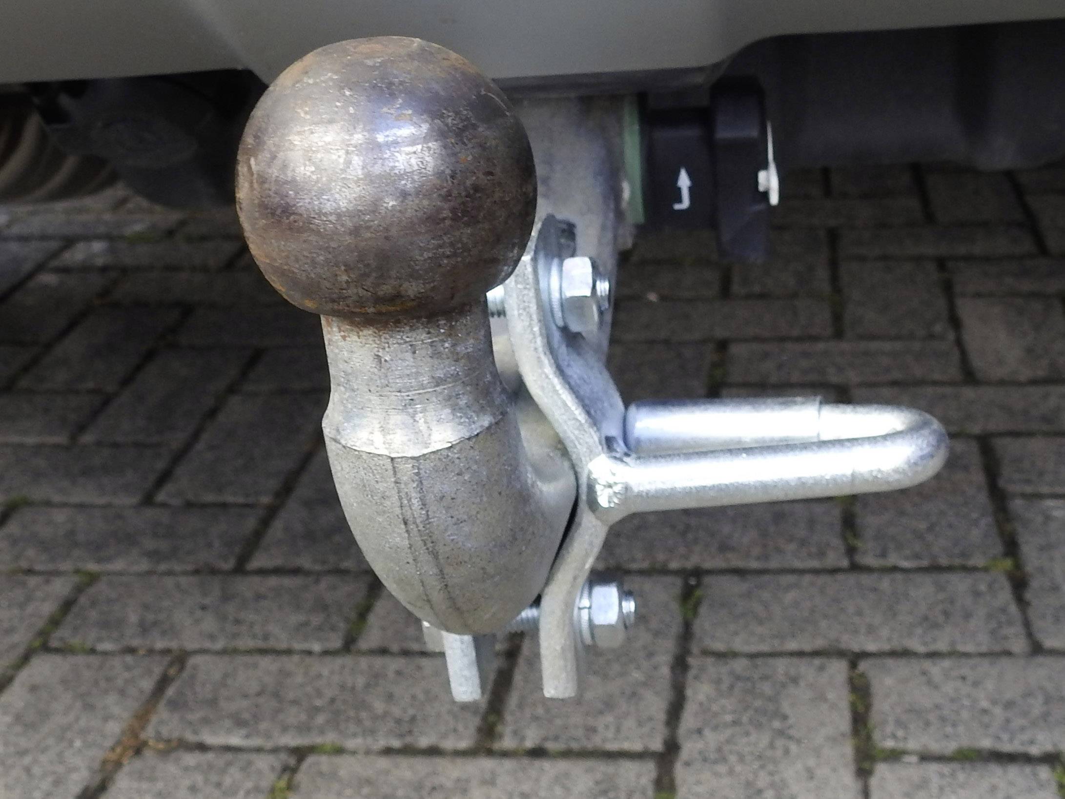 'Afneembare trekhaak bevestigd aan een auto, op een bestrate ondergrond. De koppeling is van metaal en toont een robuuste constructie.'