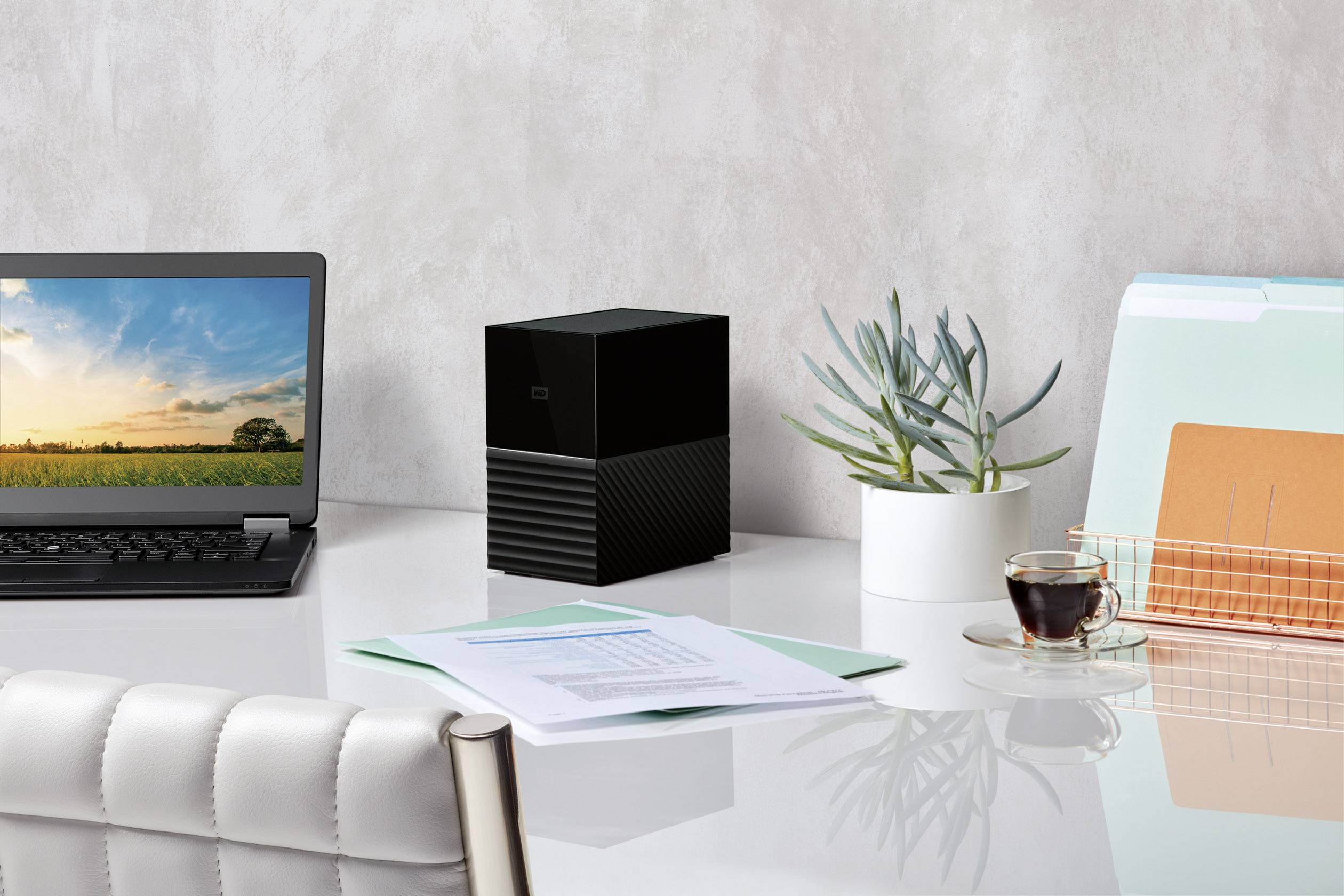 Een moderne bureau met een laptop, een kleine zwarte hardwareserver, een plant, dossiermappen en een koffiekopje.