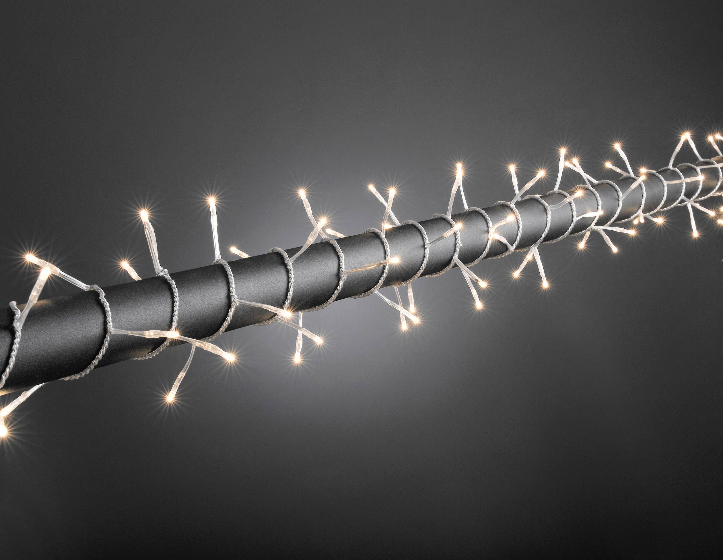 Een dunne zwarte staaf die spiraalvormig is omwikkeld met kleine, lichtgevende witte lichtjes, tegen een grijze achtergrond.