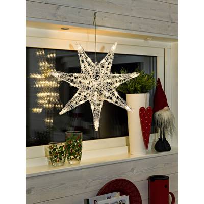 Een verlichte, transparante ster hangt voor het raam. Ernaast op de vensterbank staan twee glazen met kerstmotieven en een decoratie.