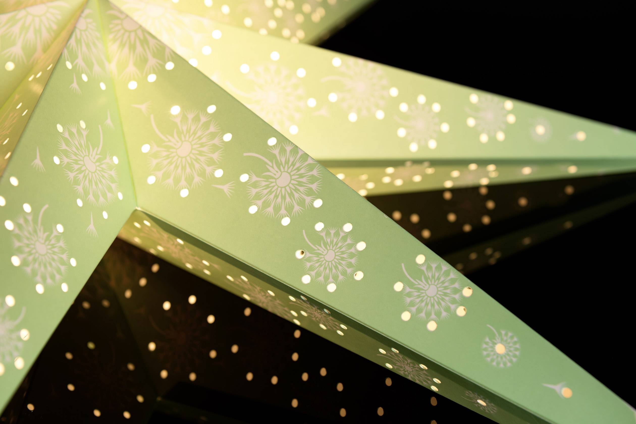 Een verlichte, decoratieve papieren ster met uitgeponste patronen schittert tegen een zwarte achtergrond.