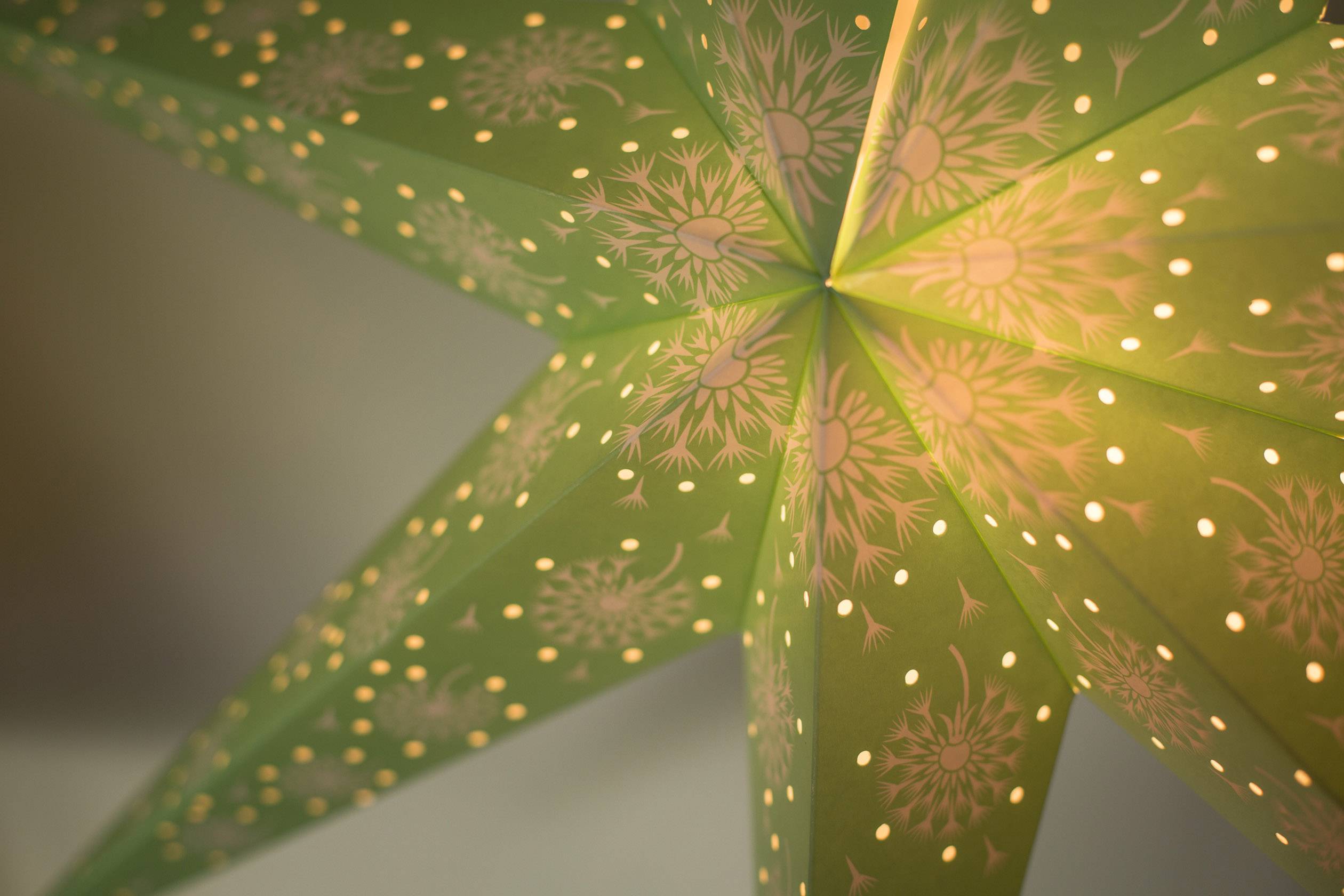 Groene papieren ster met filigrane patronen en kleine gaatjes die licht doorlaten en een decoratieve sfeer creëren.