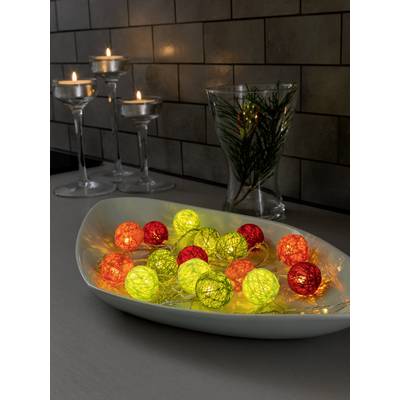 Kleurrijke slingerballetjes in een schaal op tafel, naast kaarsen en een glazen vaas met een tak, creëren een sfeervolle sfeer.