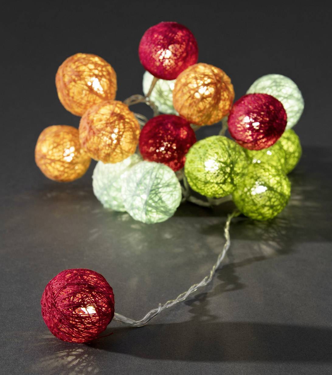 Een lichtsnoer met kleurrijke bollen van rode, oranje, groene en witte draad op een donkere achtergrond.