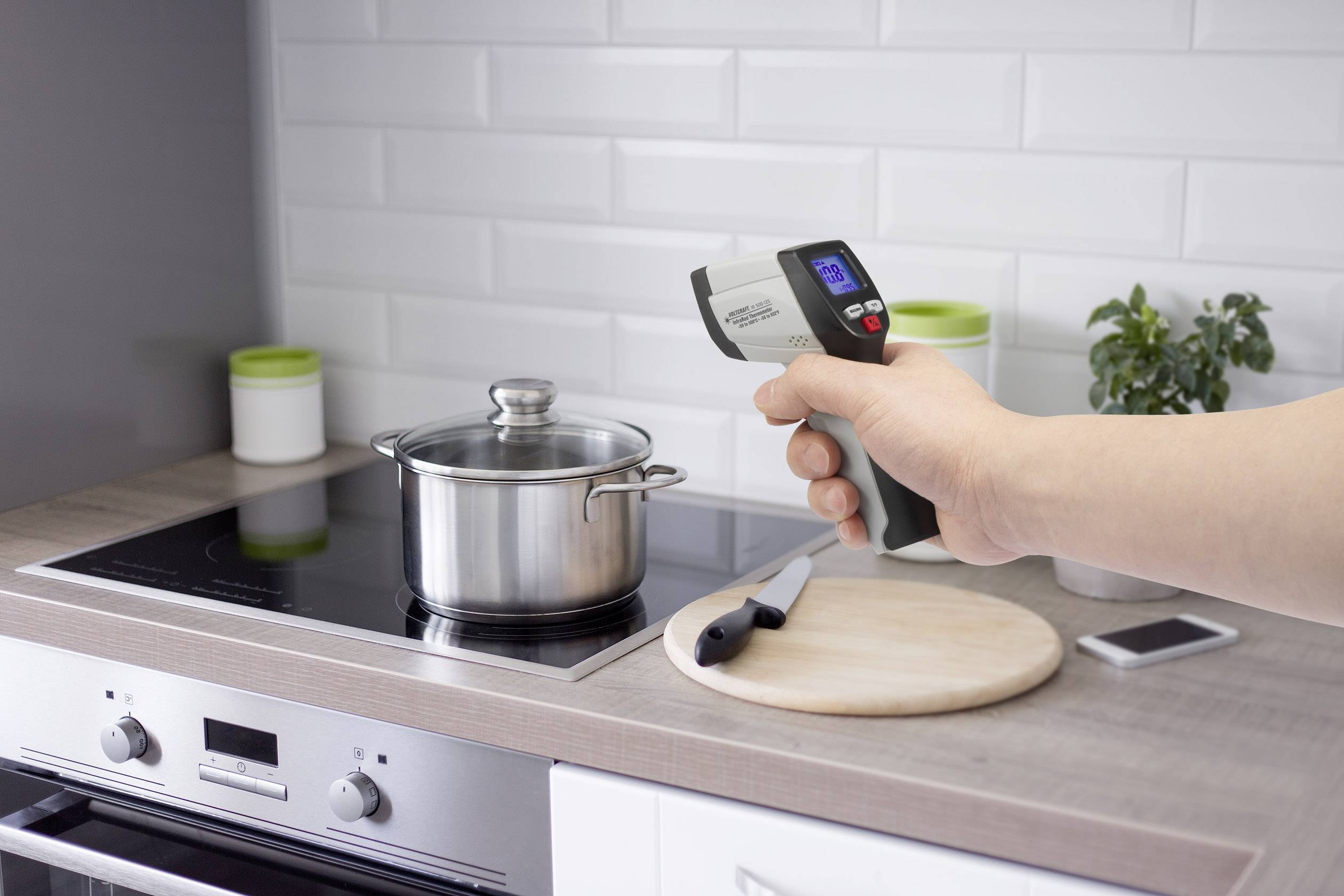 Een persoon houdt een infrarood-thermometer boven een pan op een fornuis om de temperatuur tijdens het koken te controleren.