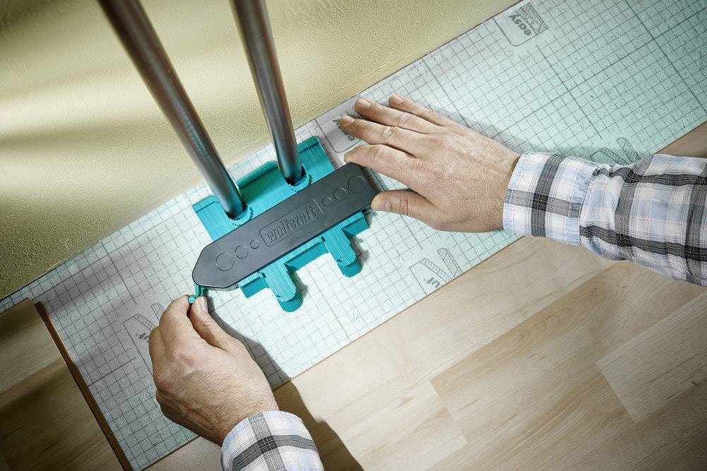 Een persoon gebruikt een gereedschap om buizen door een vloer te leiden. Het gereedschap houdt de buizen op positie op een gemarkeerd raster.