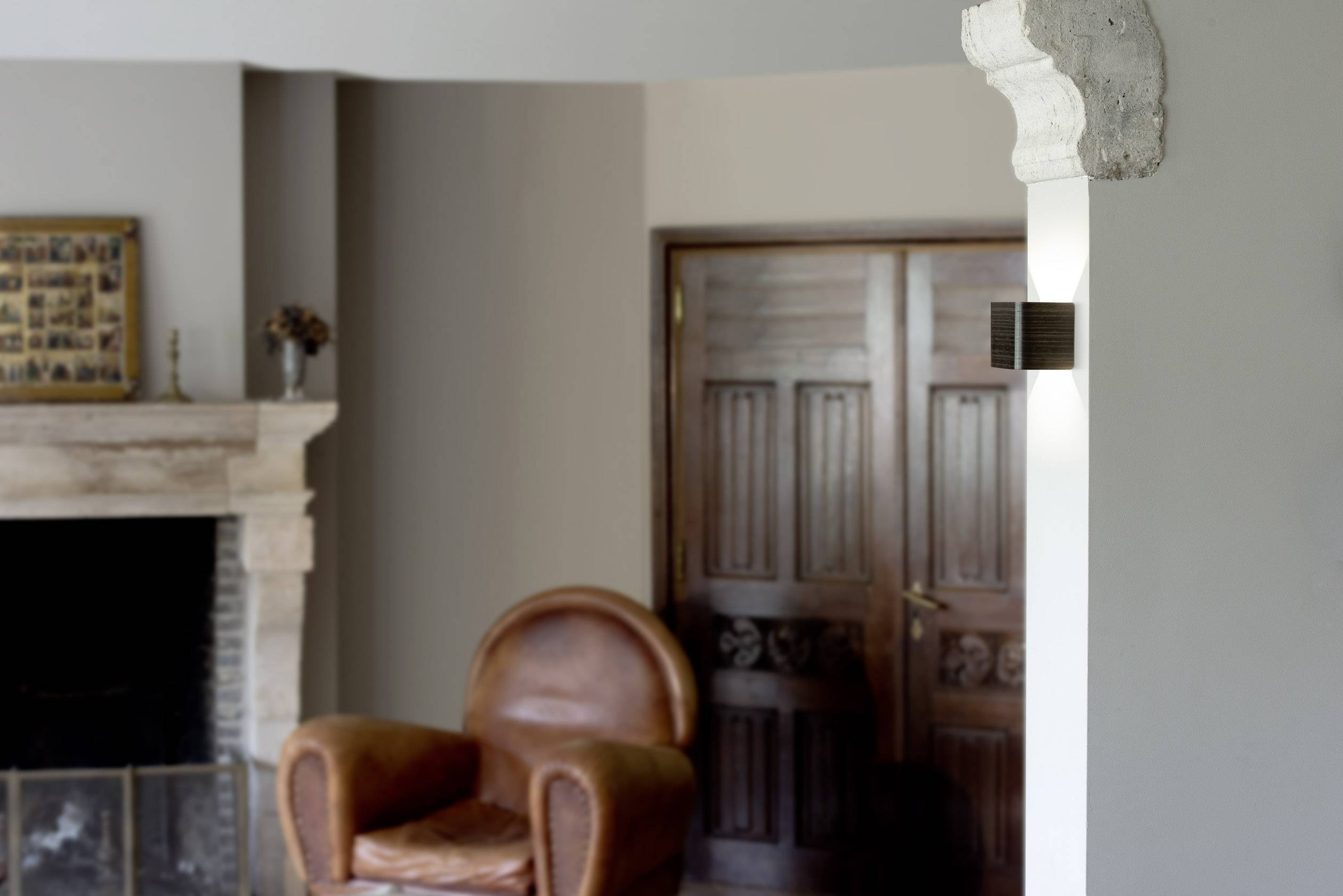 Woonkamer in neutrale tinten, met een bruine leren fauteuil, openhaard en houten deuren. Rustige sfeer met subtiele decoratie.