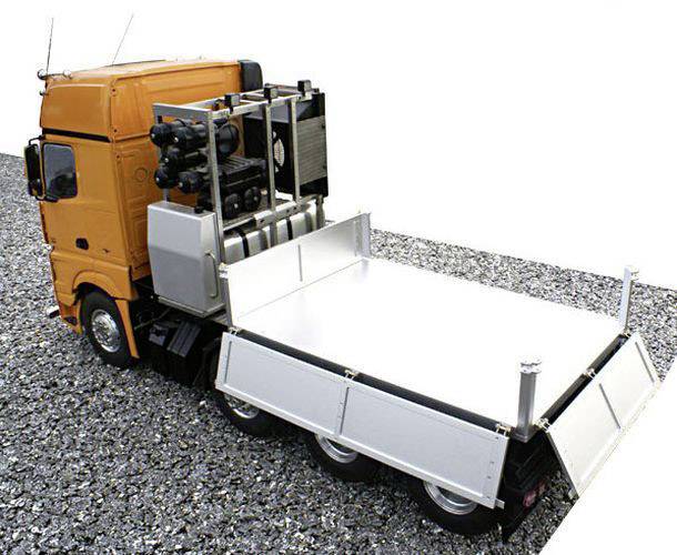 Een oranje vrachtwagen met een lege, vlakke laadruimte staat op een grindterrein.