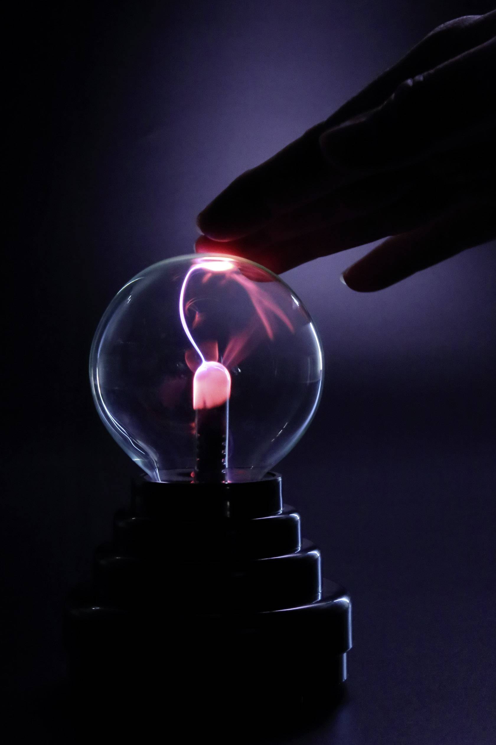 Een hand raakt een plasmabol aan, waaruit gekleurde elektrische ontladingen voortkomen die zich naar de hand toe verspreiden.