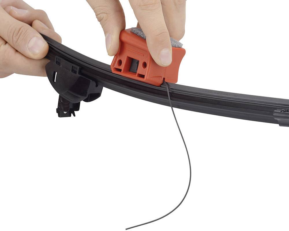 Iemand gebruikt een klein rood gereedschap om de rubberen rand van een ruitenwisser te bewerken.