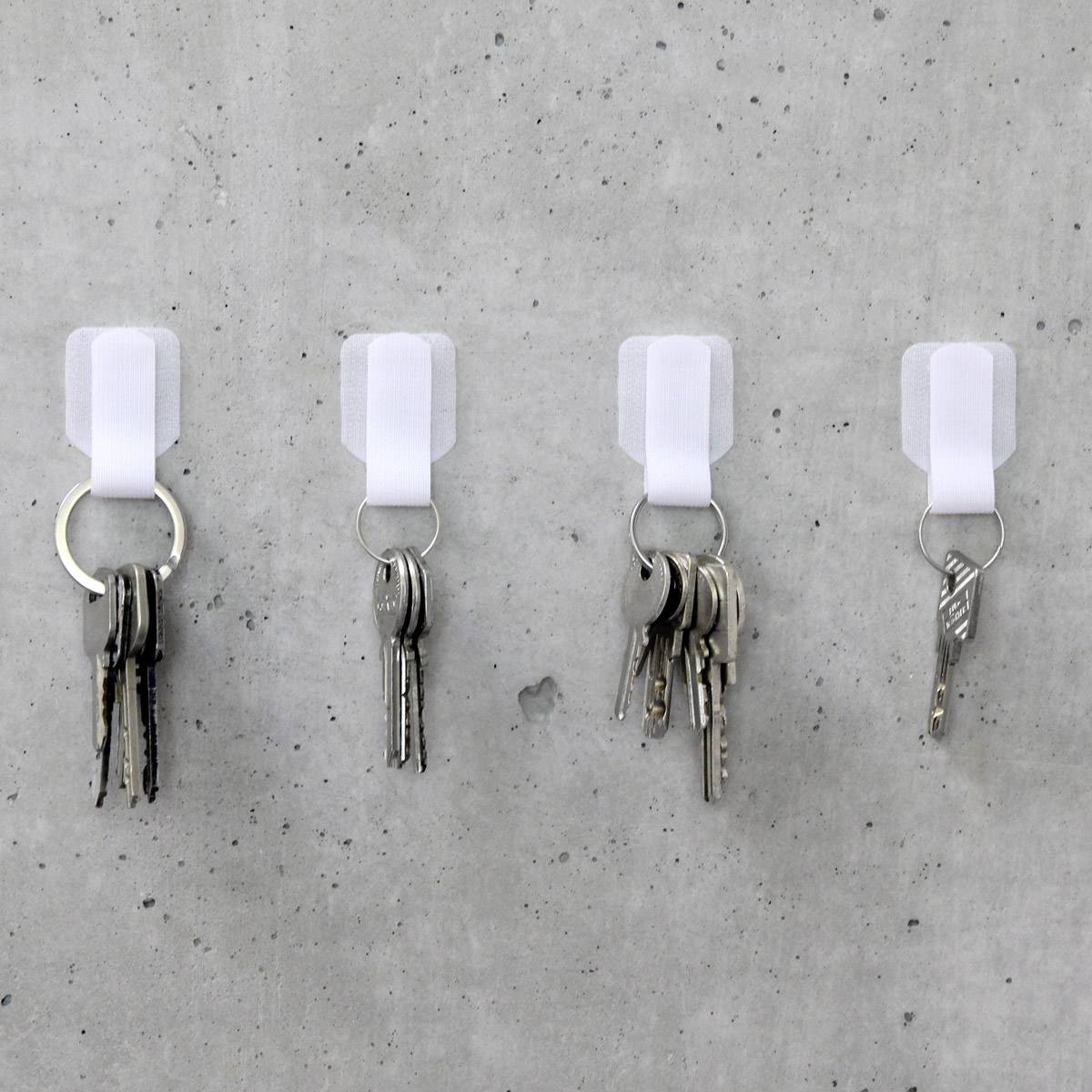 Vier sleutelhangers hangen aan witte haken aan een grijze betonnen muur. Elke sleutelbos heeft een verschillend aantal sleutels.