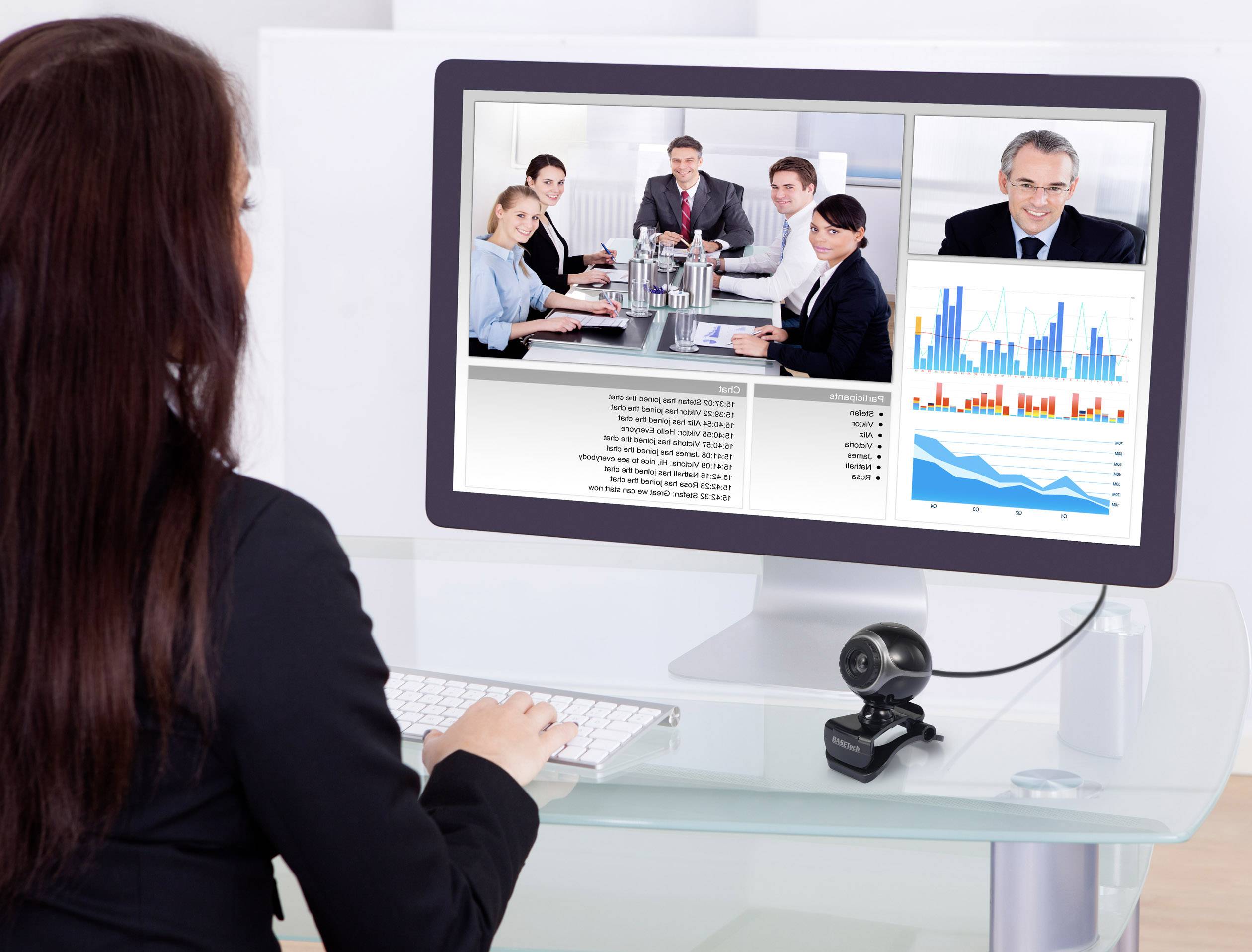 Vrouw tijdens videoconferentie aan bureau; op het scherm: vergadering met personen aan tafel en diagrammen met bedrijfsgegevens.