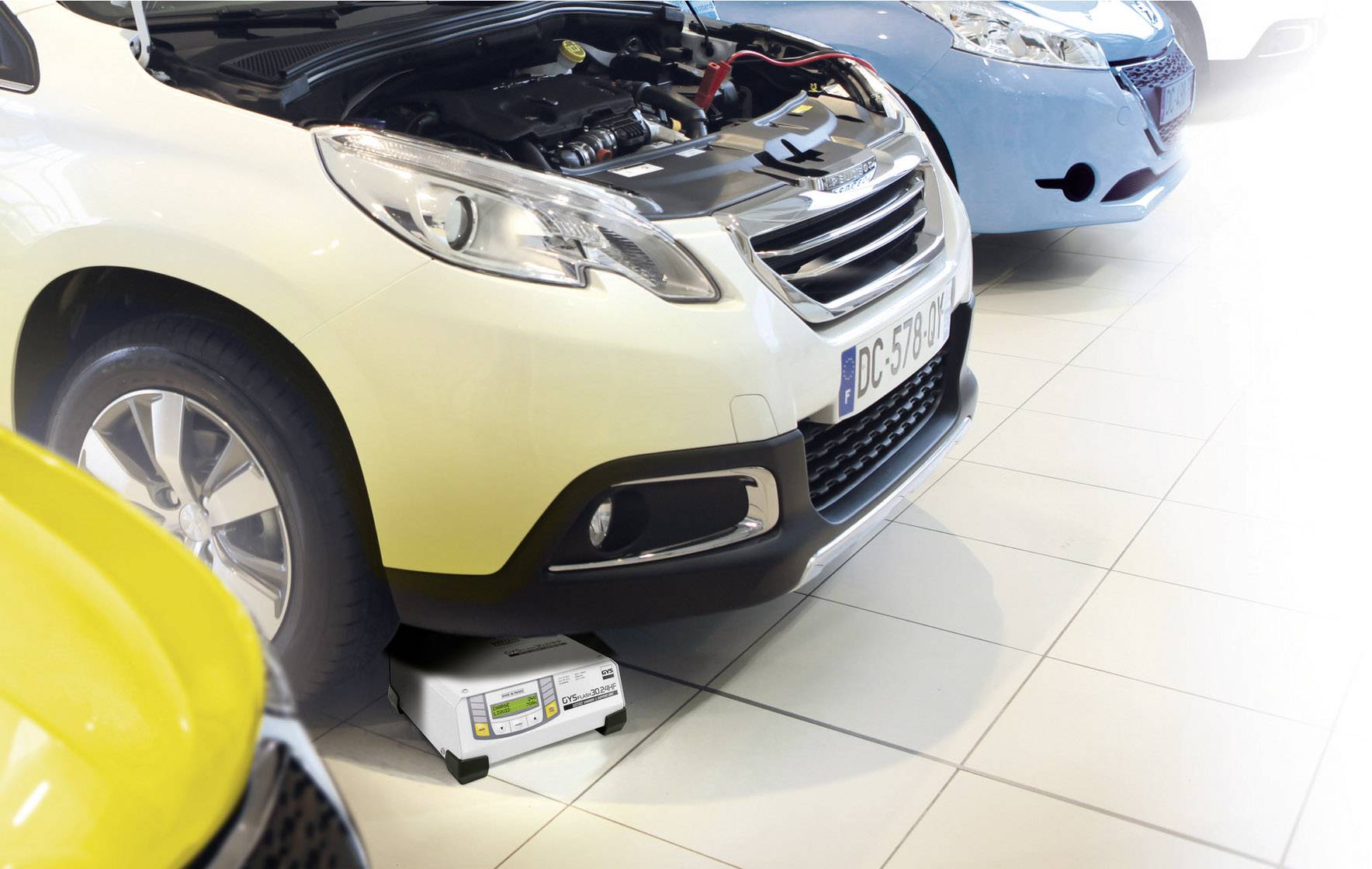 Een auto staat in een werkplaats met de motorkap open, het motordiagnoserapparaat is onderaan de auto geplaatst en controleert de accu.