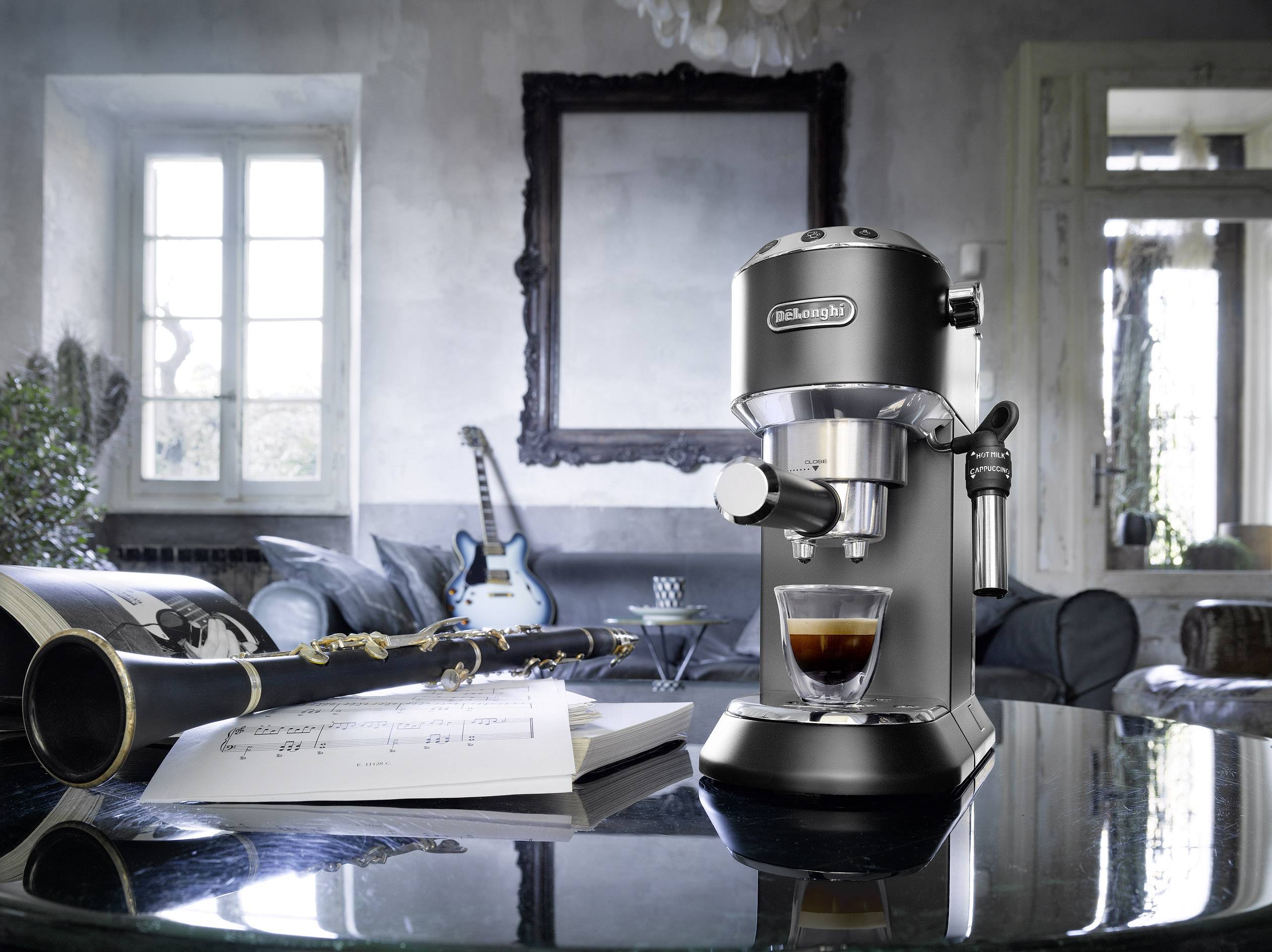 Een zwarte espressomachine op een tafel, ernaast een notitieboek, een klarinet en op de achtergrond een bank en een gitaar.