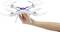 Een hand houdt een witte drone met vier rotoren in de lucht. De drone heeft blauwe en rode details op de bovenkant.