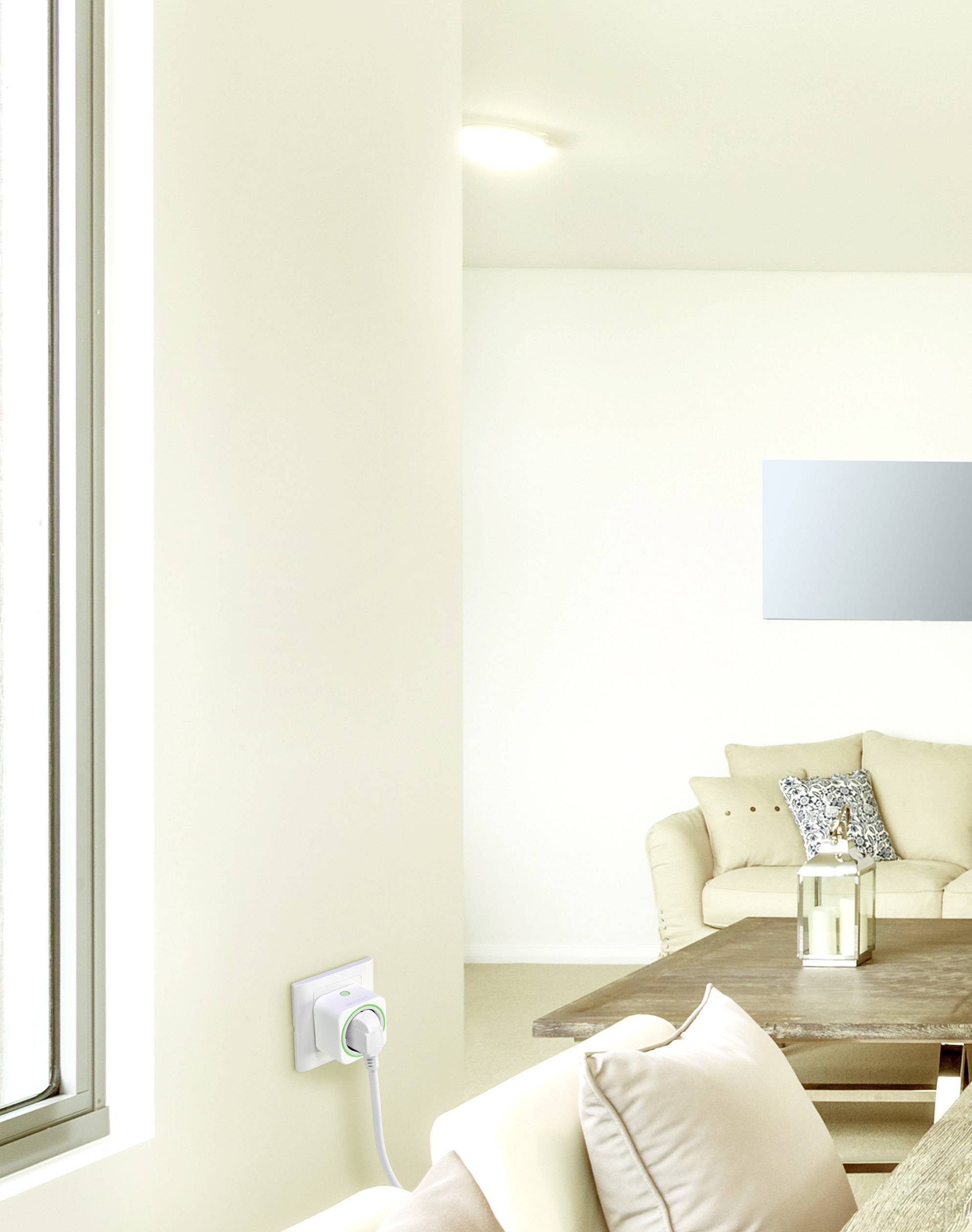 Lichte woonkamer met een beige bank en houten tafel. Een raam aan de linkerkant en een rond licht aan het plafond. Een apparaat aan de muur.