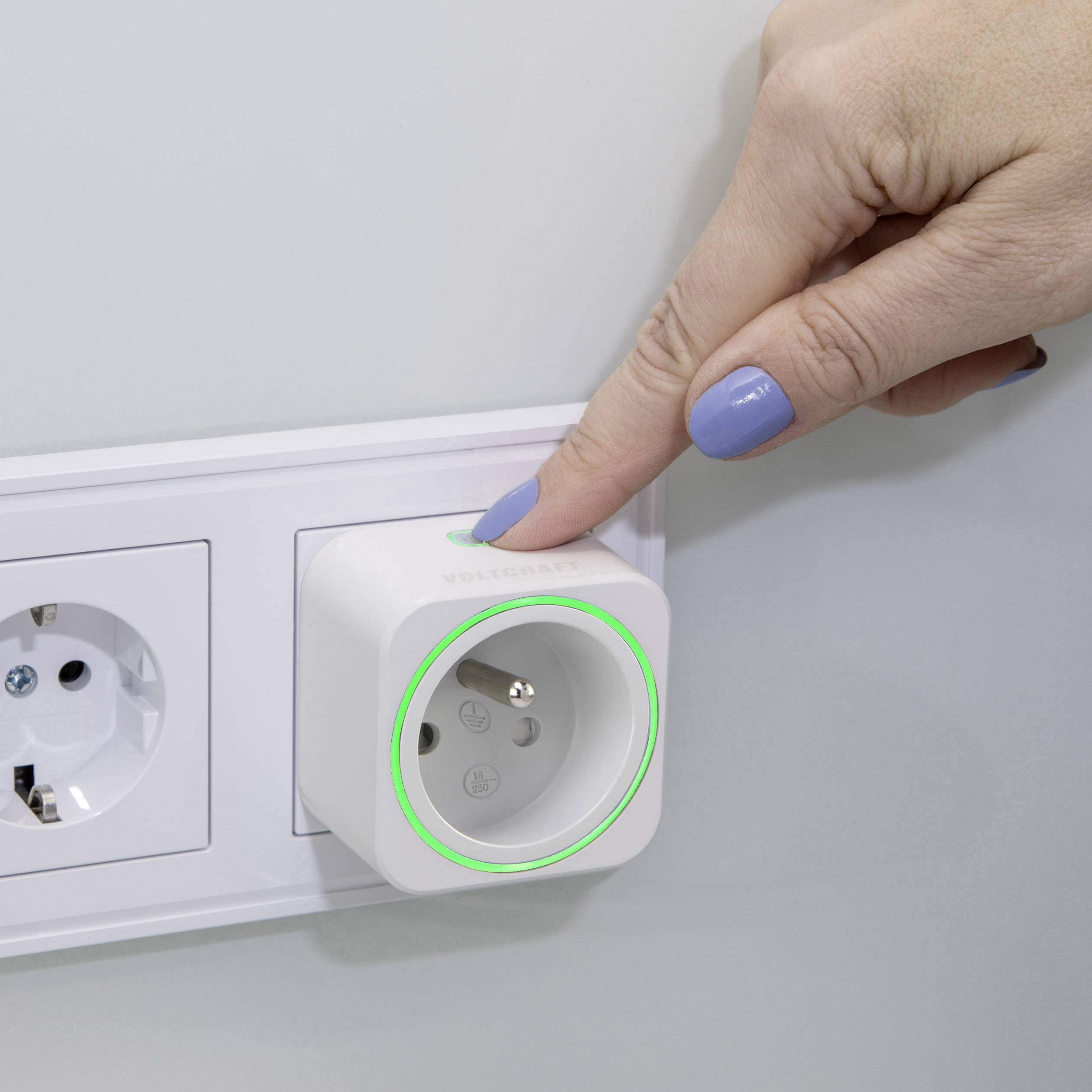 Een hand drukt op een slimme stekker die is aangesloten op een wandcontactdoos. Een groene verlichtingsring geeft aan dat het apparaat is ingeschakeld.