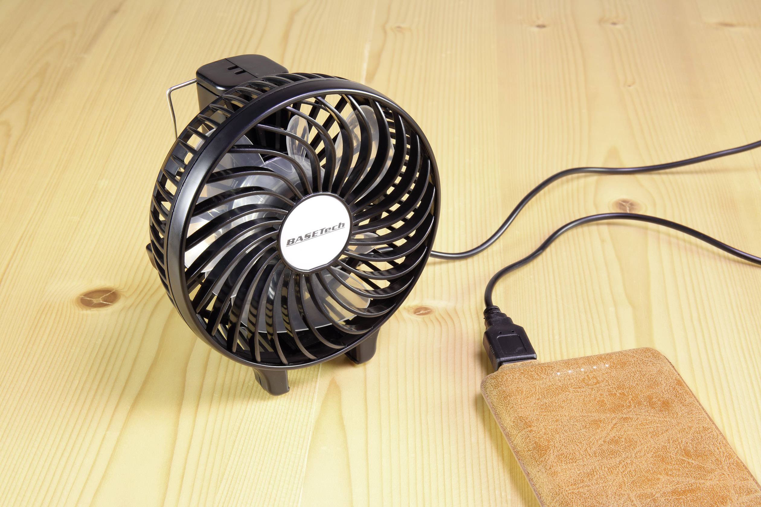 Kleine zwarte ventilator met USB-aansluiting op een houten tafel, naast een bruine powerbank.