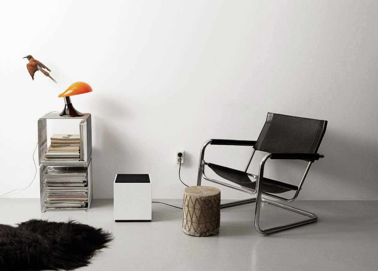 Een moderne ruimte met een zwarte stoel, een kleine houten kruk, een rek met boeken en een oranje lamp.