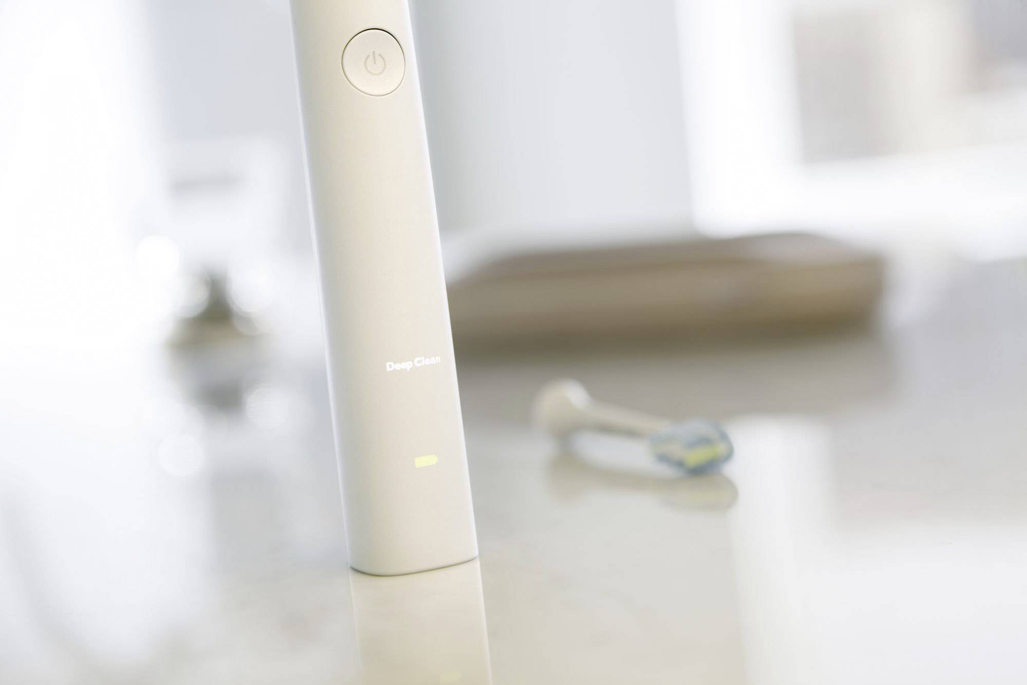 Een elektrische tandenborstel staat op een badkamerwastafel, op de achtergrond wazig een opzetstaander voor de borstenkop.