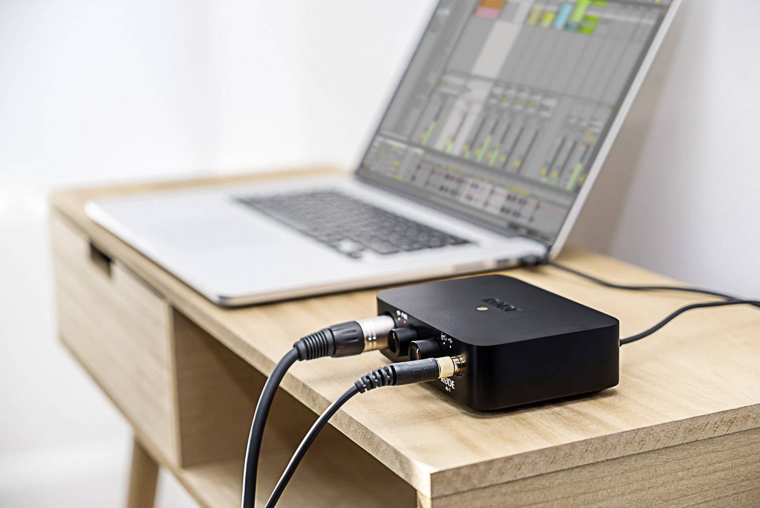 Een laptop met audiobewerkingssoftware is verbonden met een zwart audio-interface op een houten tafel.