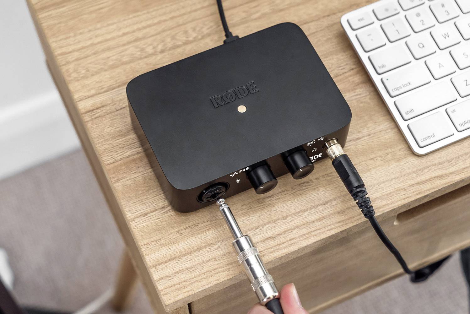 Zwart audio-interface op een bureau, verbonden met een microfoon en een computer, toont een actieve LED-lamp.