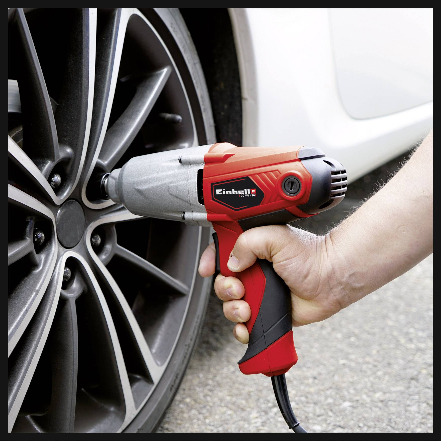 Een hand gebruikt een rode elektrische slagschroevendraaier om een wielmoer aan een autoband vast te draaien.