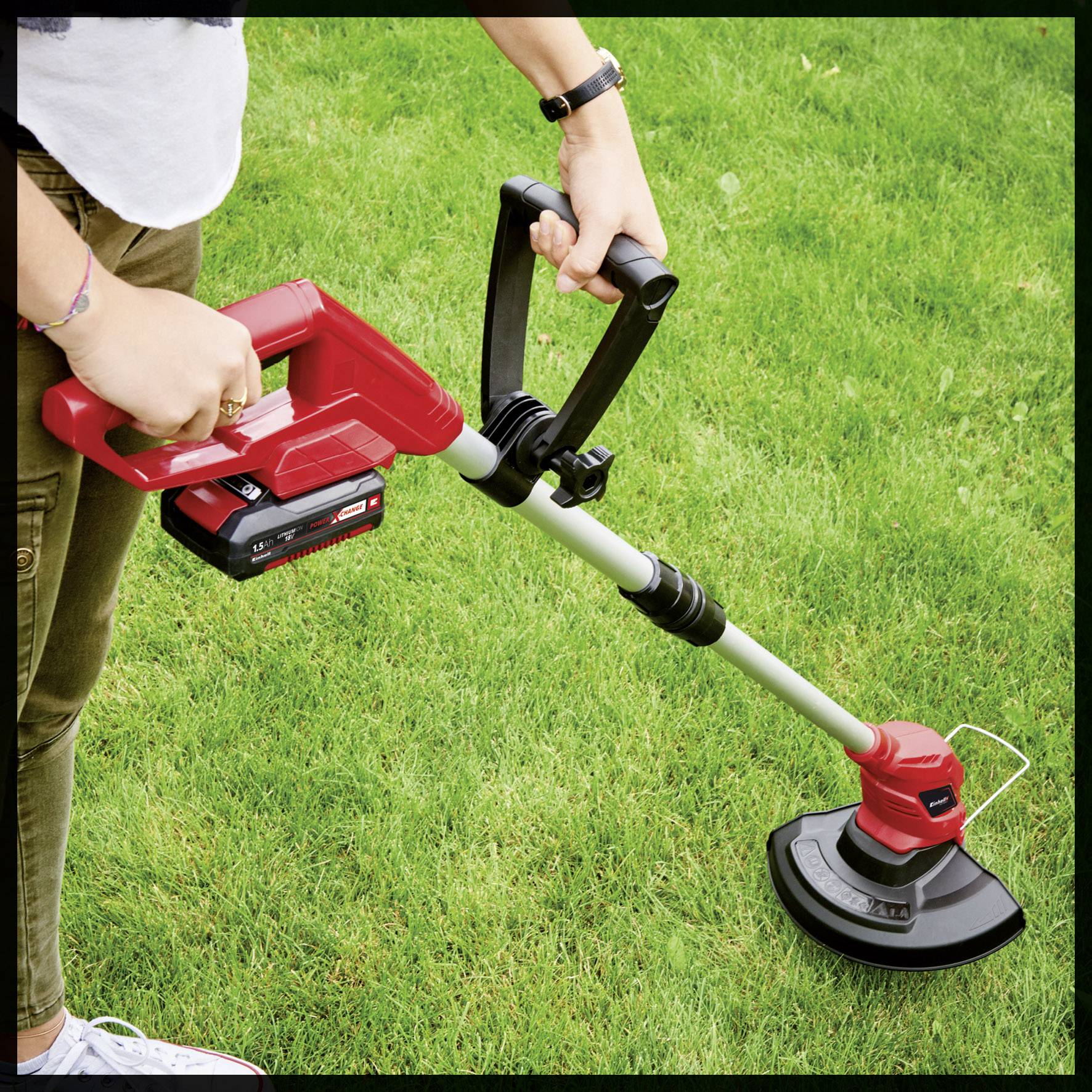 Een persoon maait het gras in de tuin met een rode, elektrische grastrimmer. De accuvan het apparaat is aan de trimmer bevestigd.