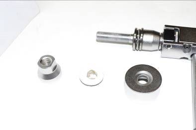 Een montagepistool met een plug, schroef en sluitring op een witte ondergrond. De onderdelen liggen naast elkaar.