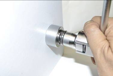 Een persoon gebruikt een moersleutel om een ronde metalen schroef vast te draaien op een witte oppervlakte.