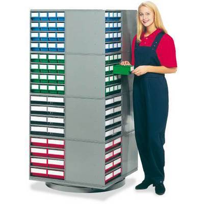 Vrouw in een rood shirt en blauwe overall staat naast een grijs rekensysteem met kleurrijke laden en houdt een groene doos vast.