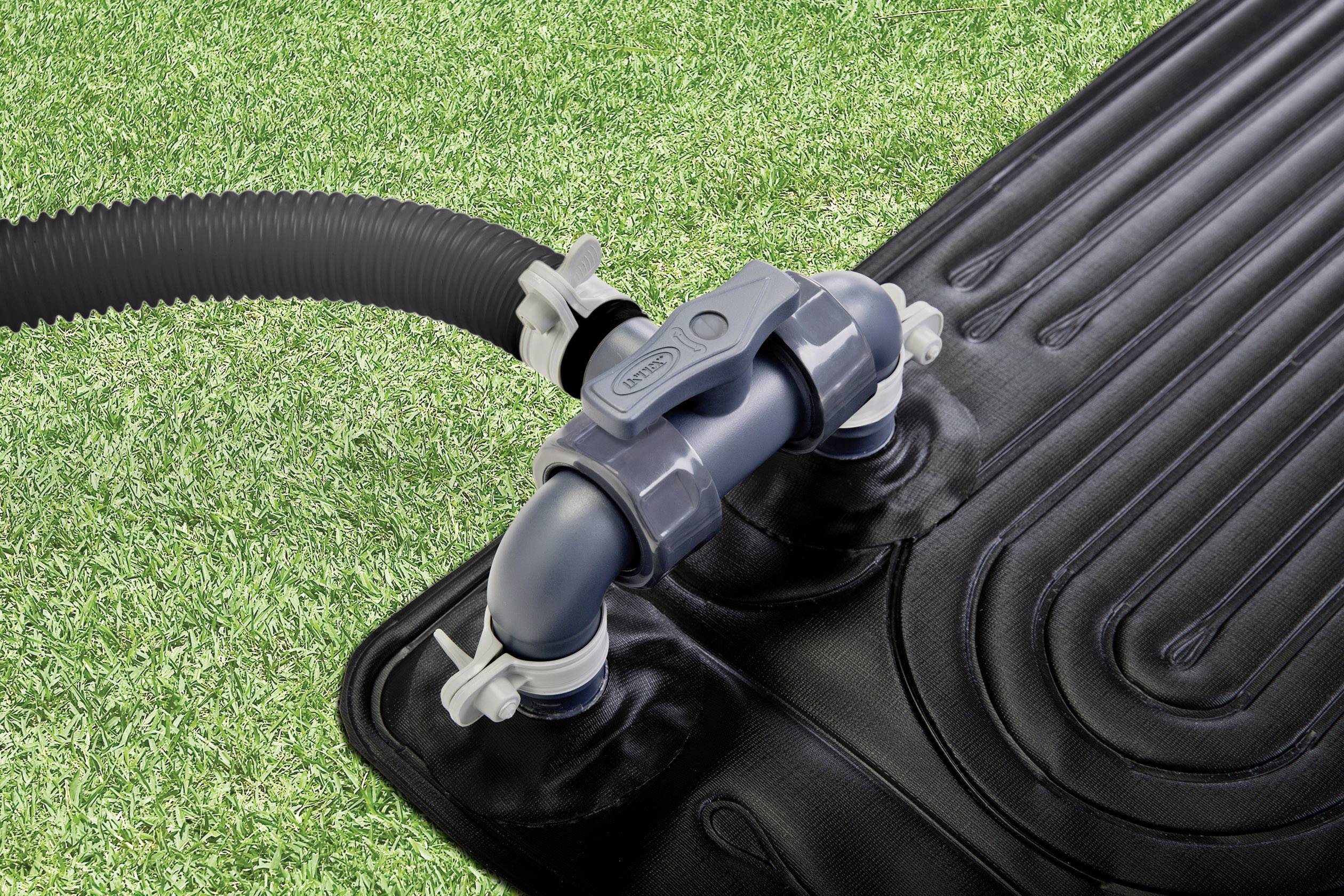 Een zwarte zonnecollector met spiraalvormige buizen op een grasveld. Een grijze slang is aangesloten op de collector.