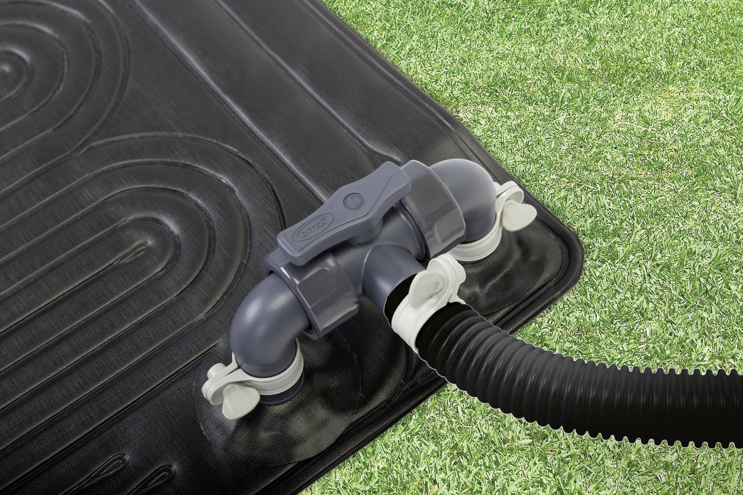 Tuinslang aangesloten op een zonne-energieverwarmingssysteem op groen gazon; toont verbindingselementen in close-up.