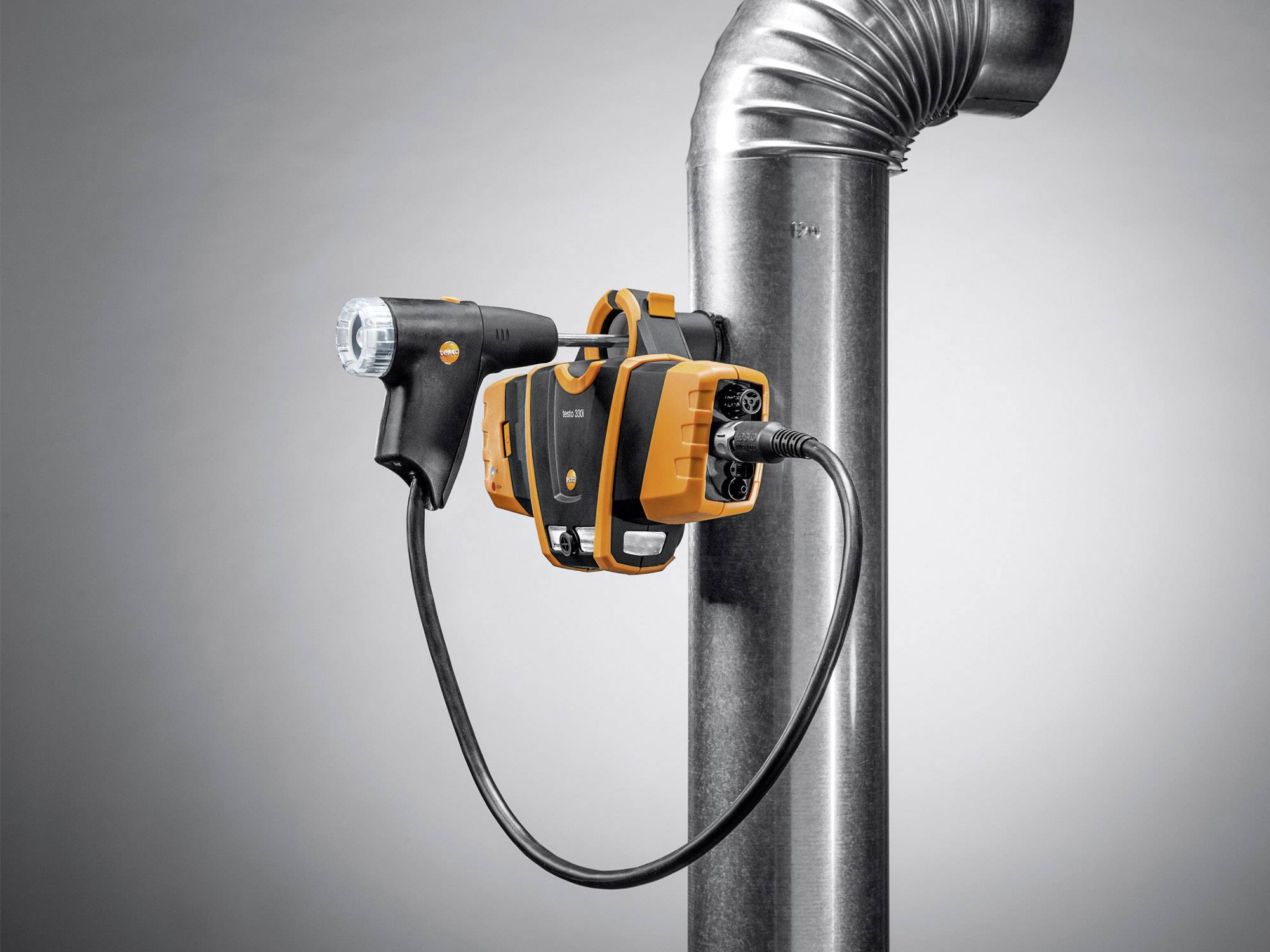 Een oranje-zwart apparaat is bevestigd aan een metalen buis. Het lijkt een inspectieapparaat te zijn met een camera aan een flexibel kabel.