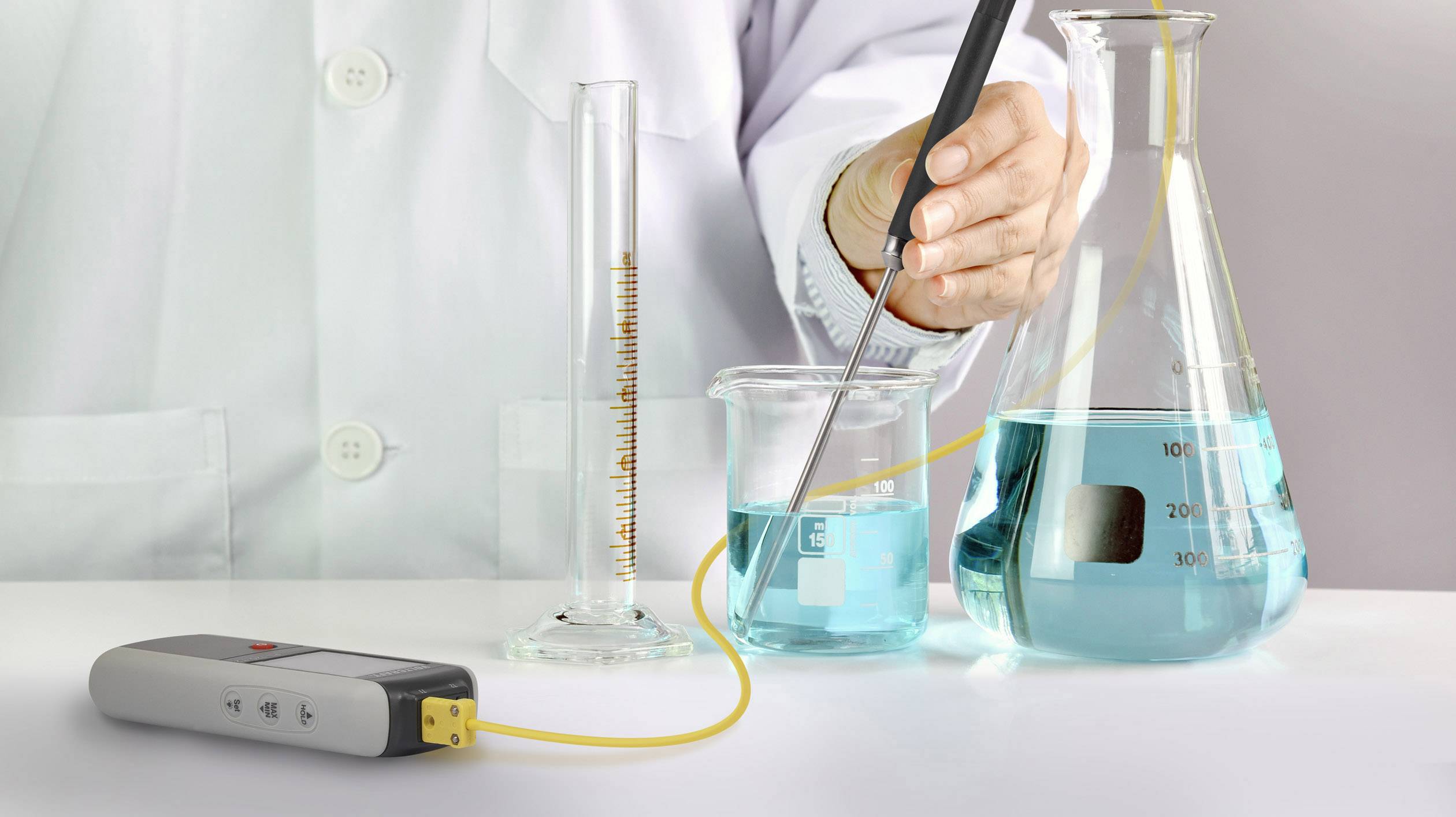 Een persoon in een laboratoriumjas meet de pH-waarde van een blauwe vloeistof in een bekerglas met een meetapparaat.