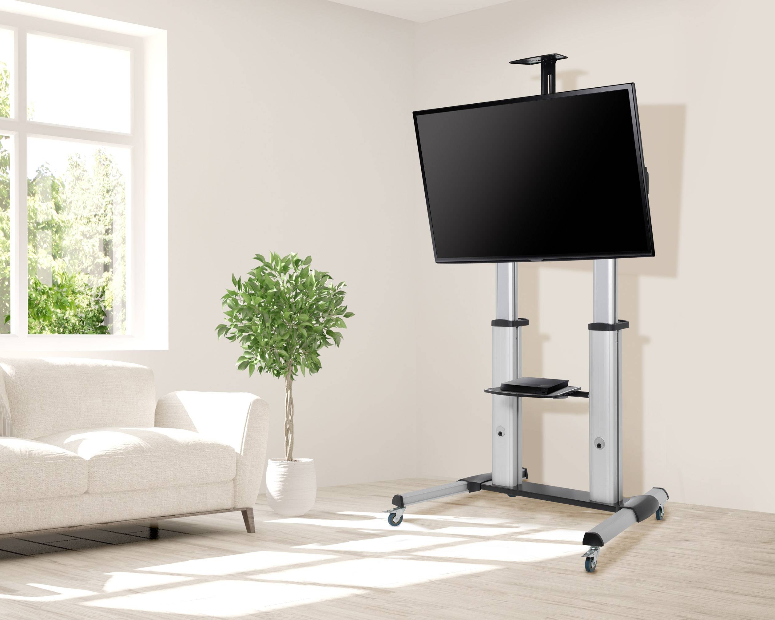 Een scherm op een mobiele standaard in een woonkamer naast een bank en een plant. Lichte, lichtovergoten omgeving.