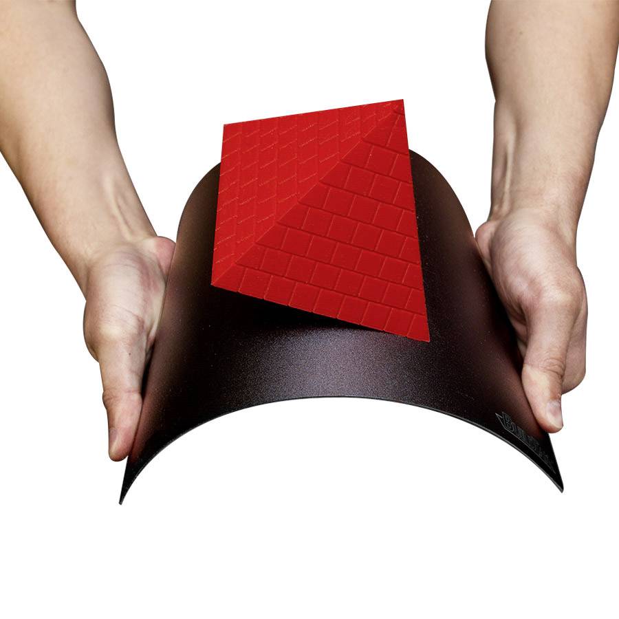 Twee handen houden een zwart doek of mat vast, waarop een rode, driehoekige 3D-constructie staat.