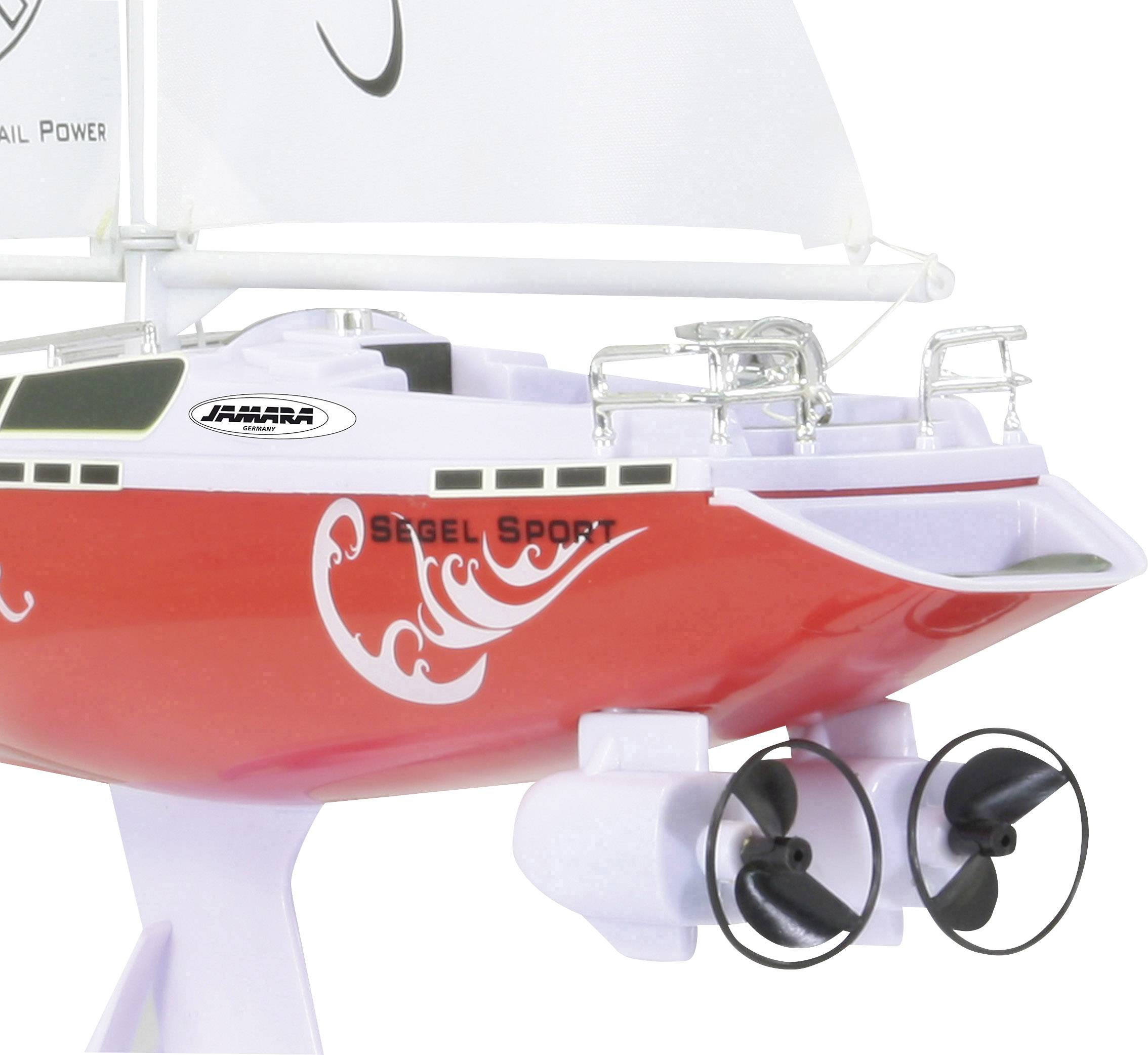 Speelgoed zeilboot in rood en wit met motor, opgetrokken zeilen en gedrukte teksten.