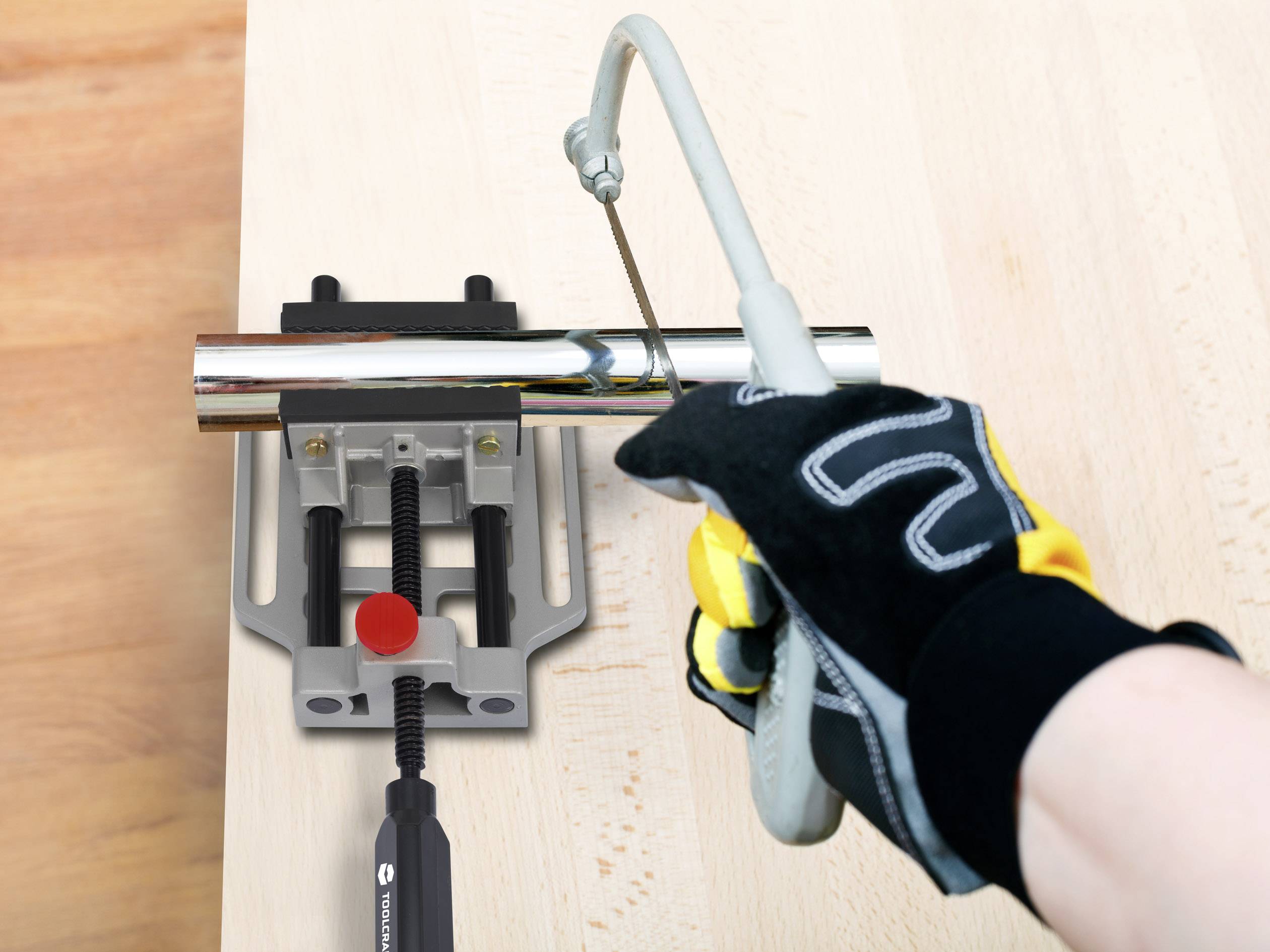 Een persoon met handschoenen zaagt een metalen buis door met een beugzaag op een tafel. De buis is vastgeklemd in een bankschroef.