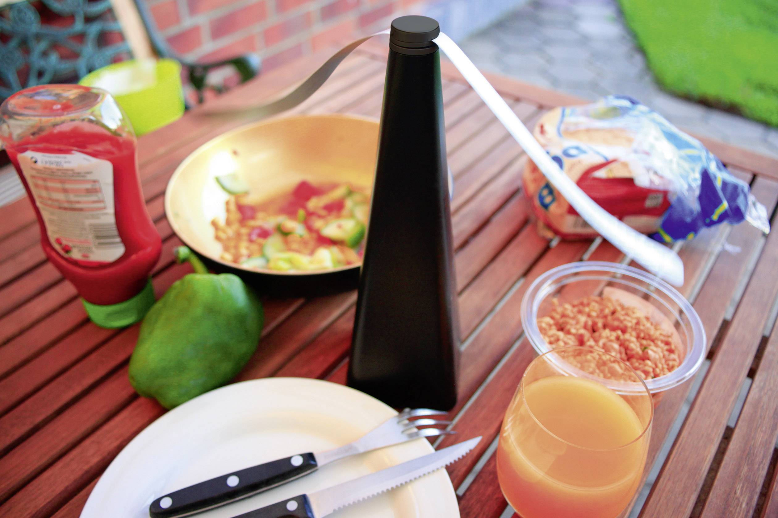 Een gedekte tafel met een bord, bestek, glas sinaasappelsap, pan met groenten, ketchupfles, brood en onandgesneden fruit.