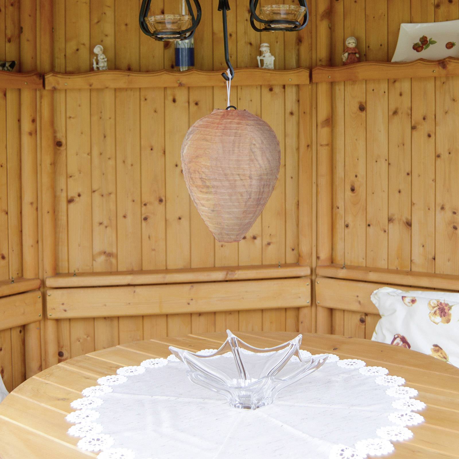 Een rustiek ontworpen houten tuinpaviljoen met een ronde tafel, gedecoreerd met een wit tafelkleed en een glazen schaal eronder.