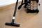 Een persoon reinigt een houten vloer met een zwarte stofzuiger. De ruimte ziet er schoon en netjes uit.