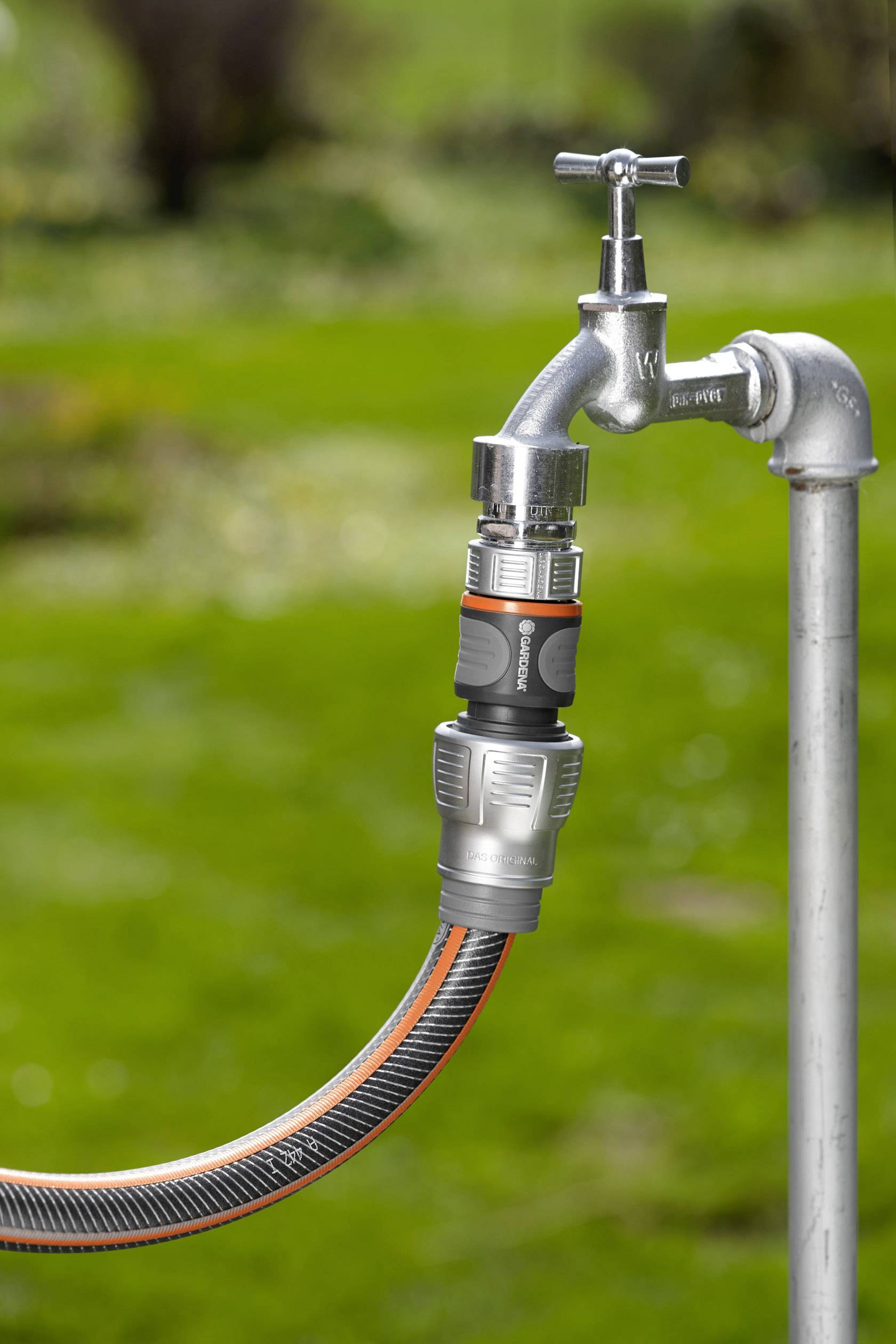 Een zilveren buitenkraan met daaraan een tuinslang met een oranje-grijze aansluiting, tegen een groene achtergrond.