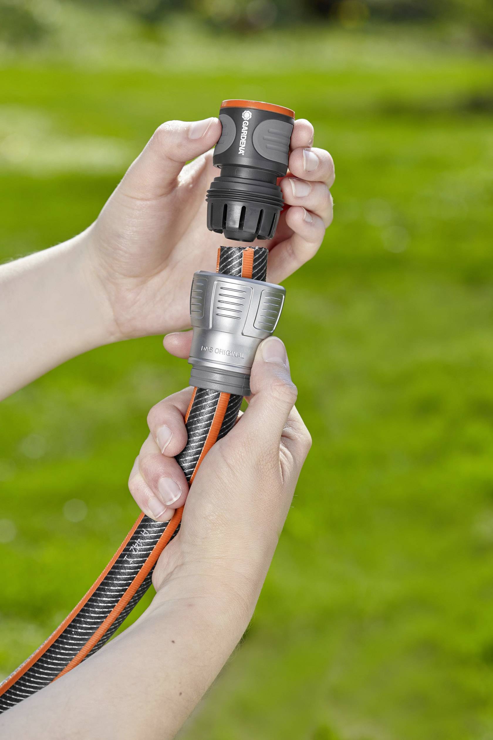 Twee handen verbinden een tuinslangstuk met een steekadapter op een groen gazon.