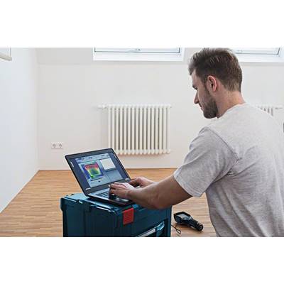 Een man werkt met een laptop aan een warmtebeeldopname van een kamer. Op de achtergrond is een radiator zichtbaar.
