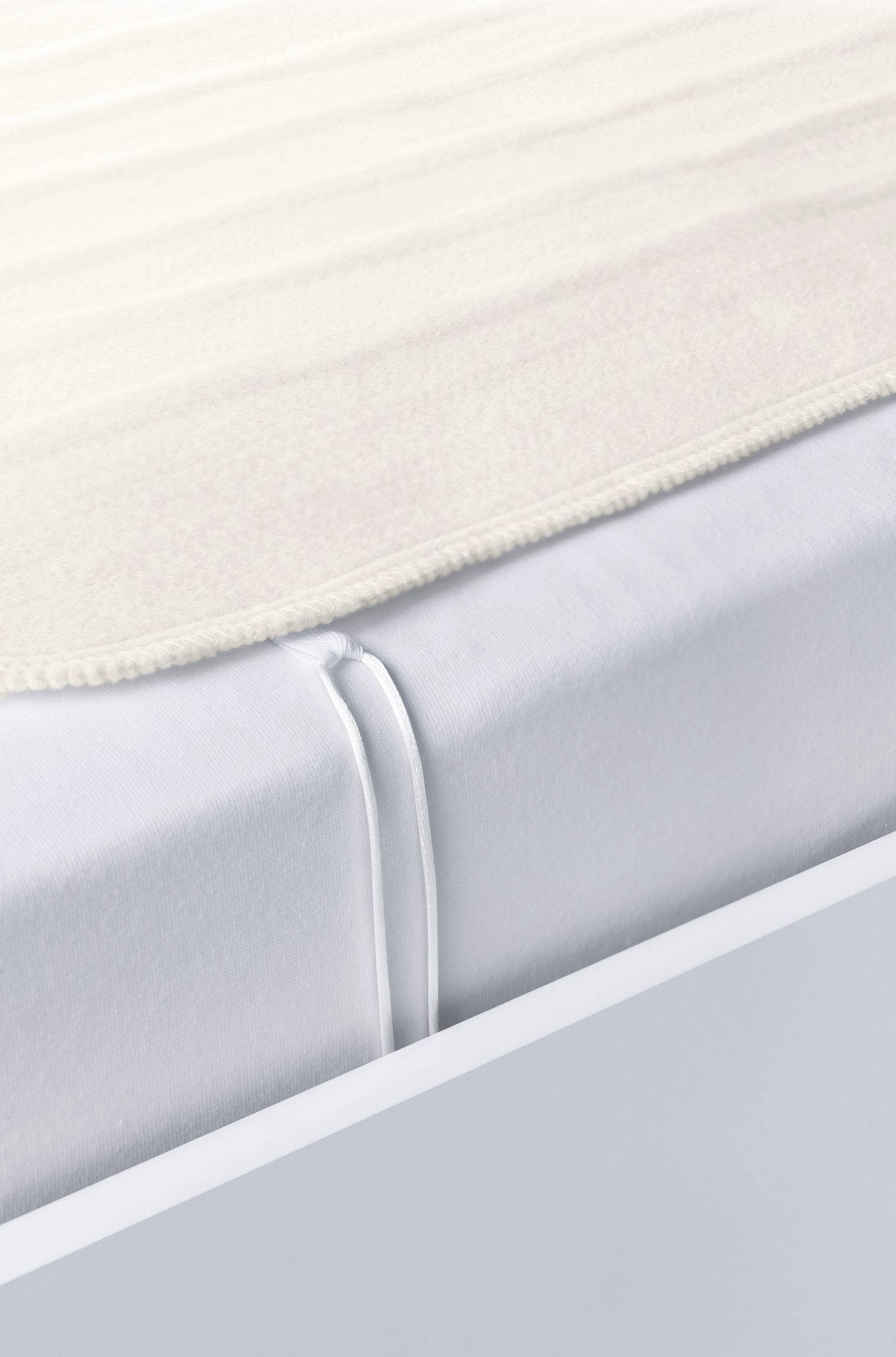 Een close-up van een bed met een wit hoeslaken en een beige deken, toont de gladde en nette bedopmaken.